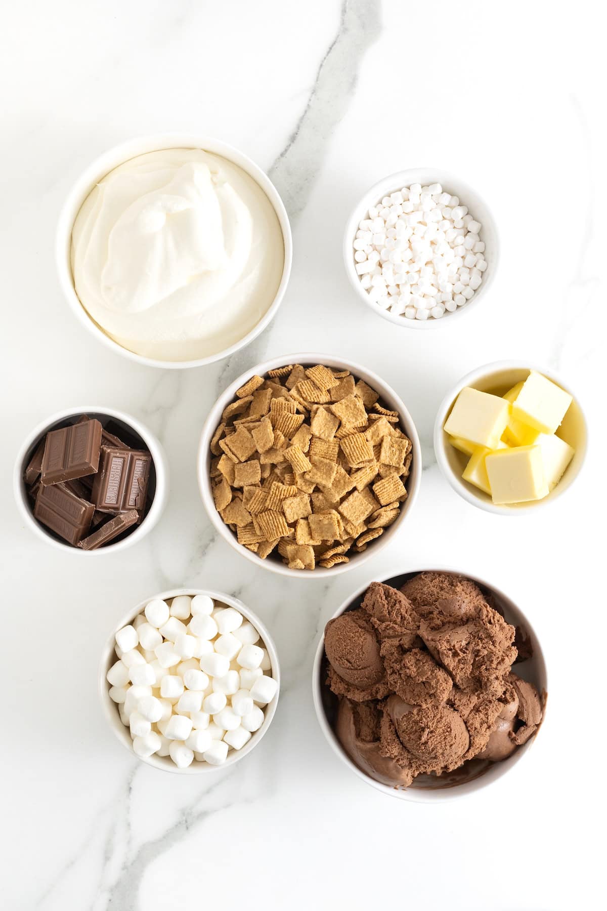 Ingredients to make S'mores Ice Cream Cake in small white dishes on a white marble counter.