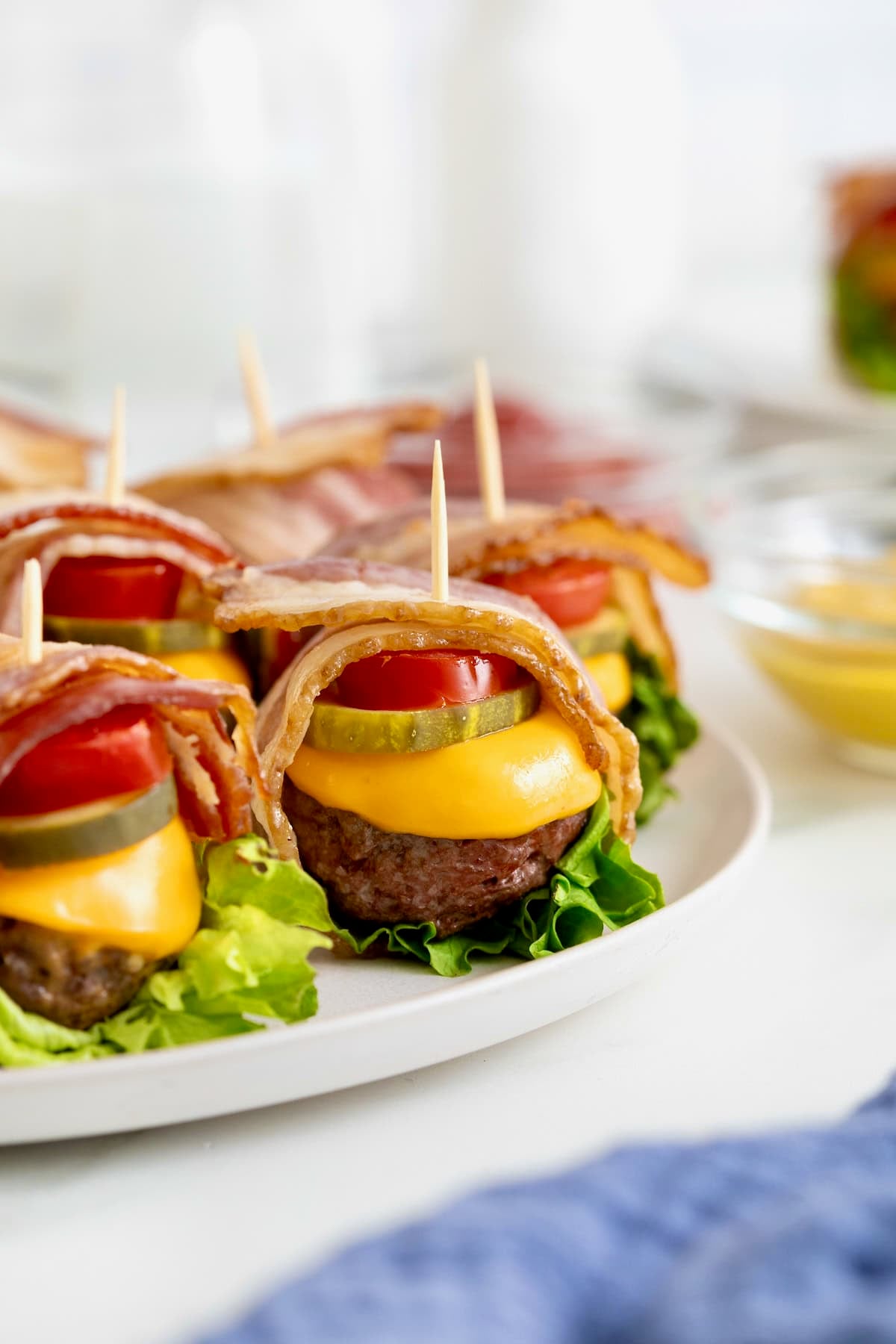 Six bacon wrapped cheese burger bites on a white platter.