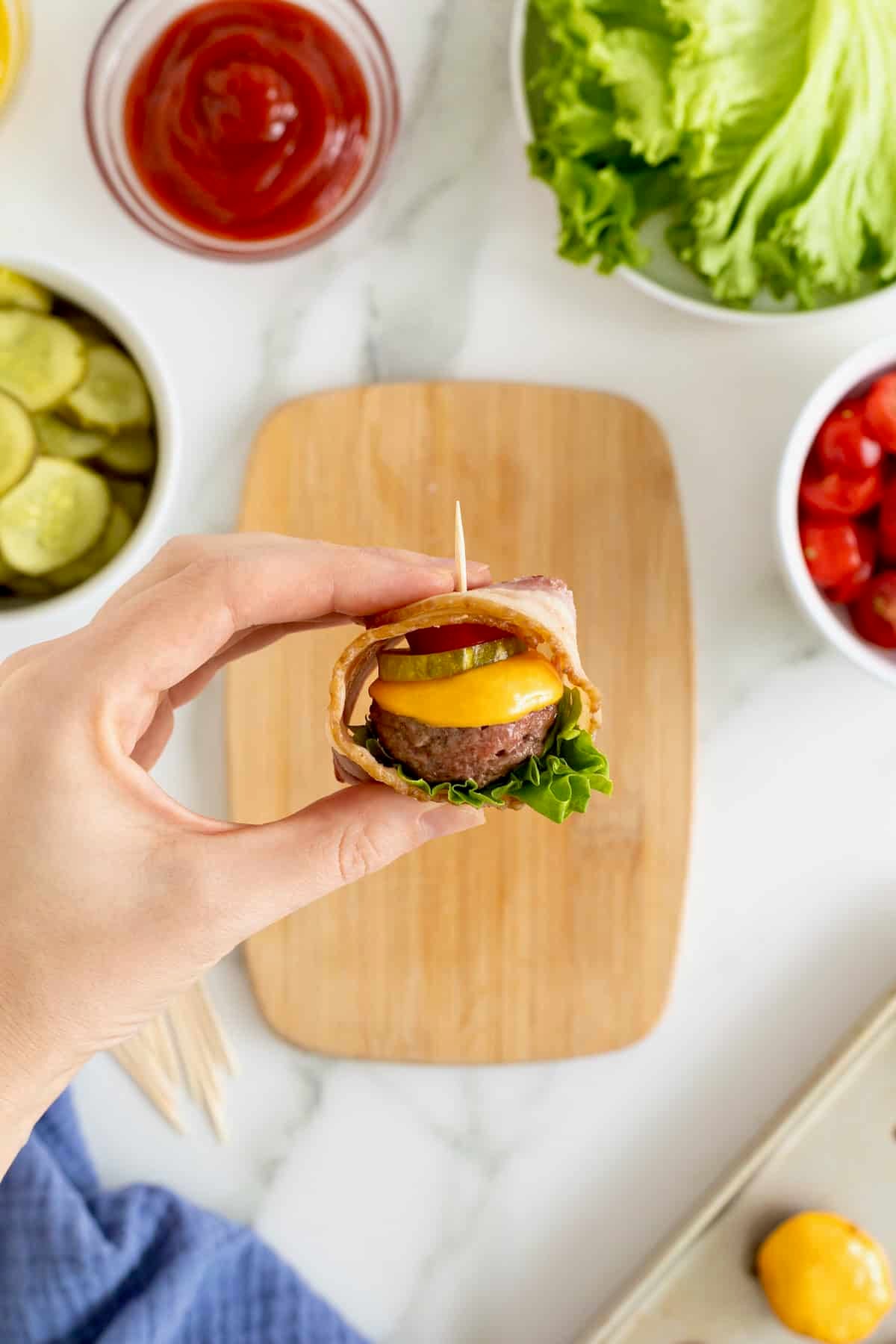 A hand holding a cheeseburger bite over a wood cutting board.