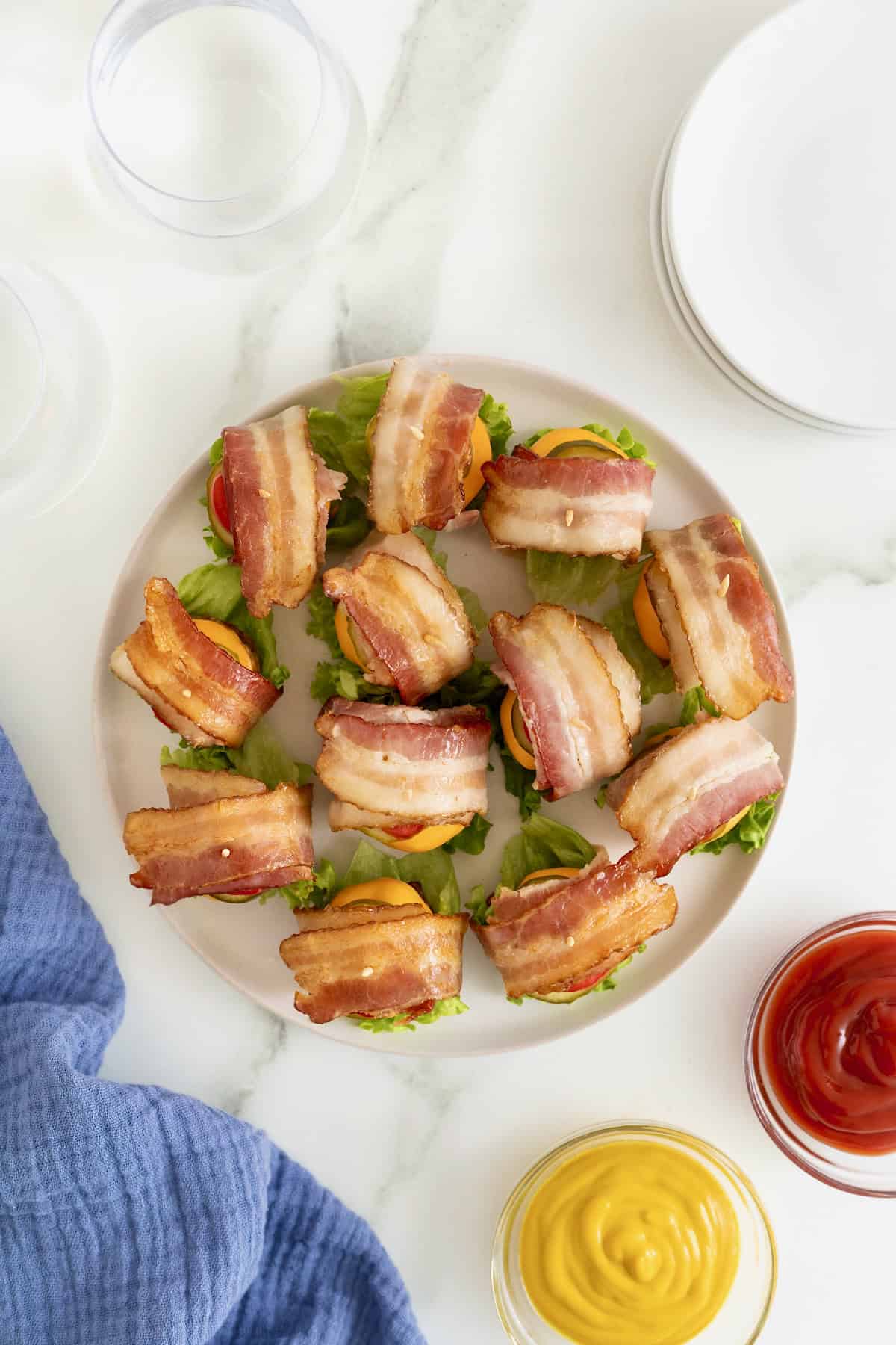 A dozen mini bacon wrapped cheeseburgers on a white platter.