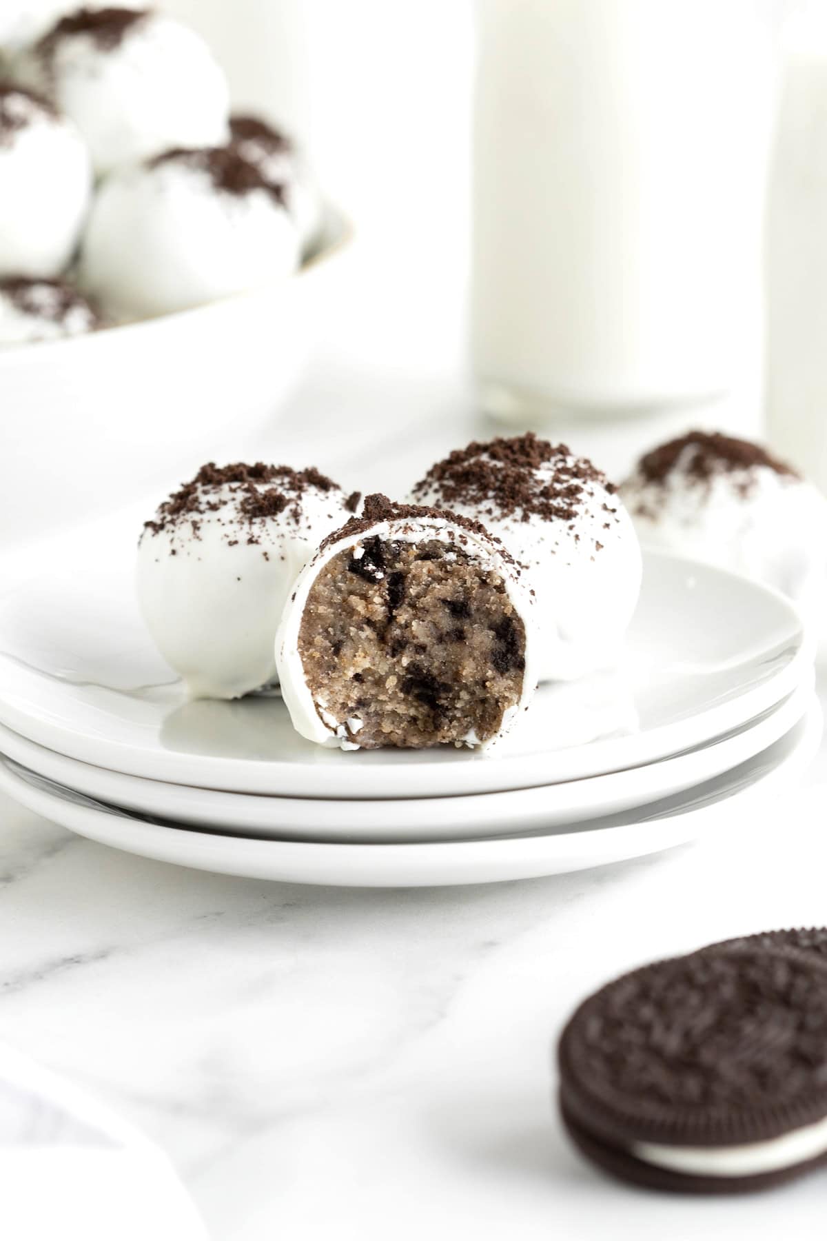 There Oreo cake balls on a stack of three white plates. The front cake ball has a bite out of it.