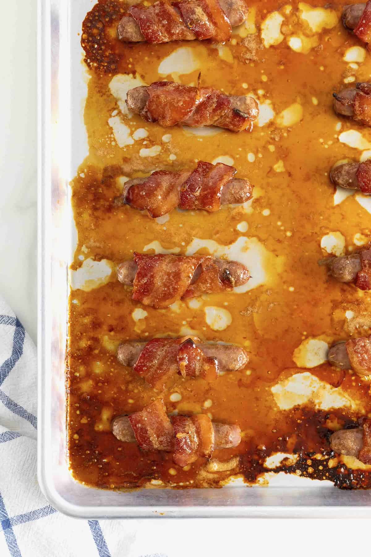 Bacon-wrapped sausages secured by toothpicks on an aluminum baking tray.