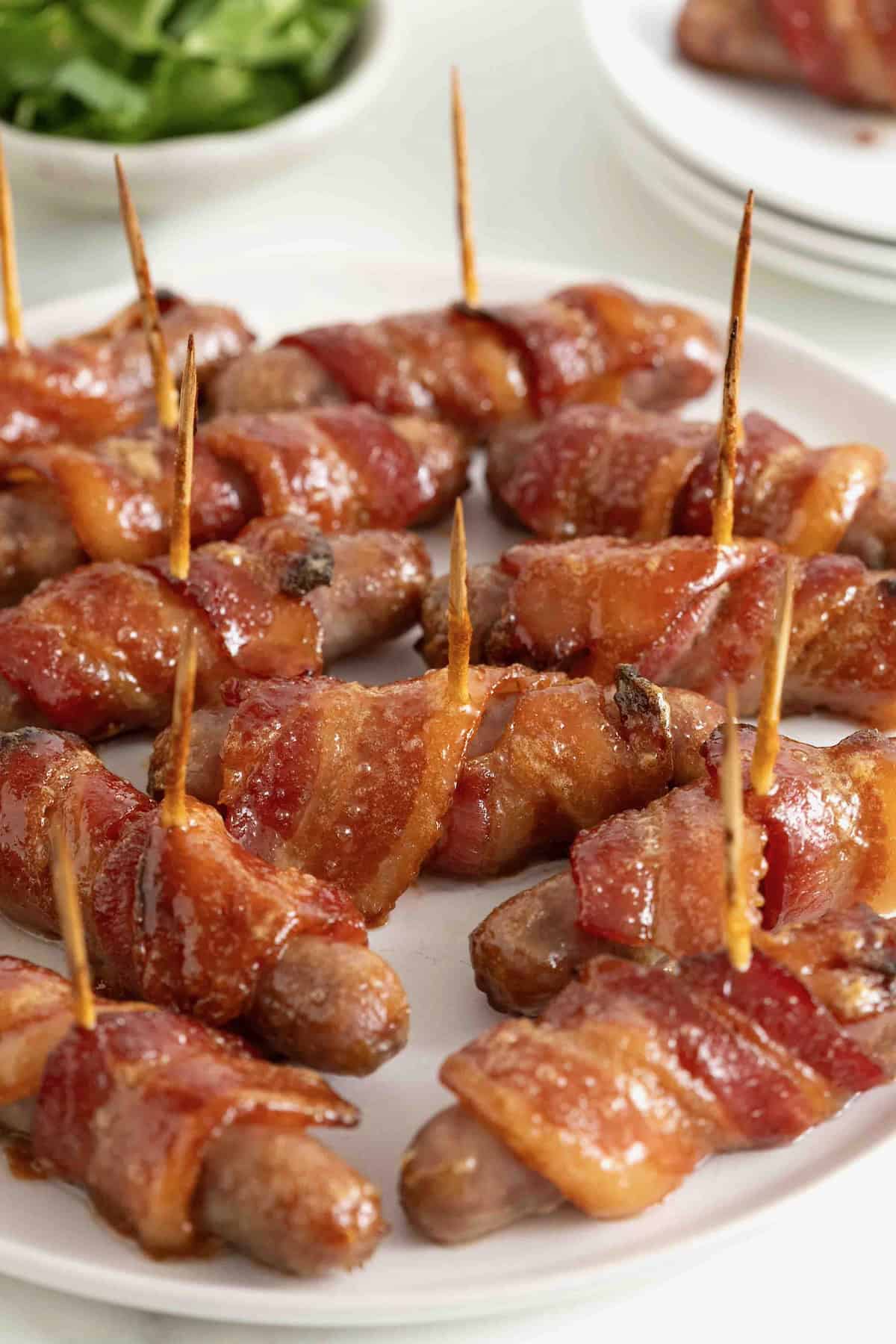 A white serving platter of breakfast sausages wrapped in bacon and secured with toothpicks.