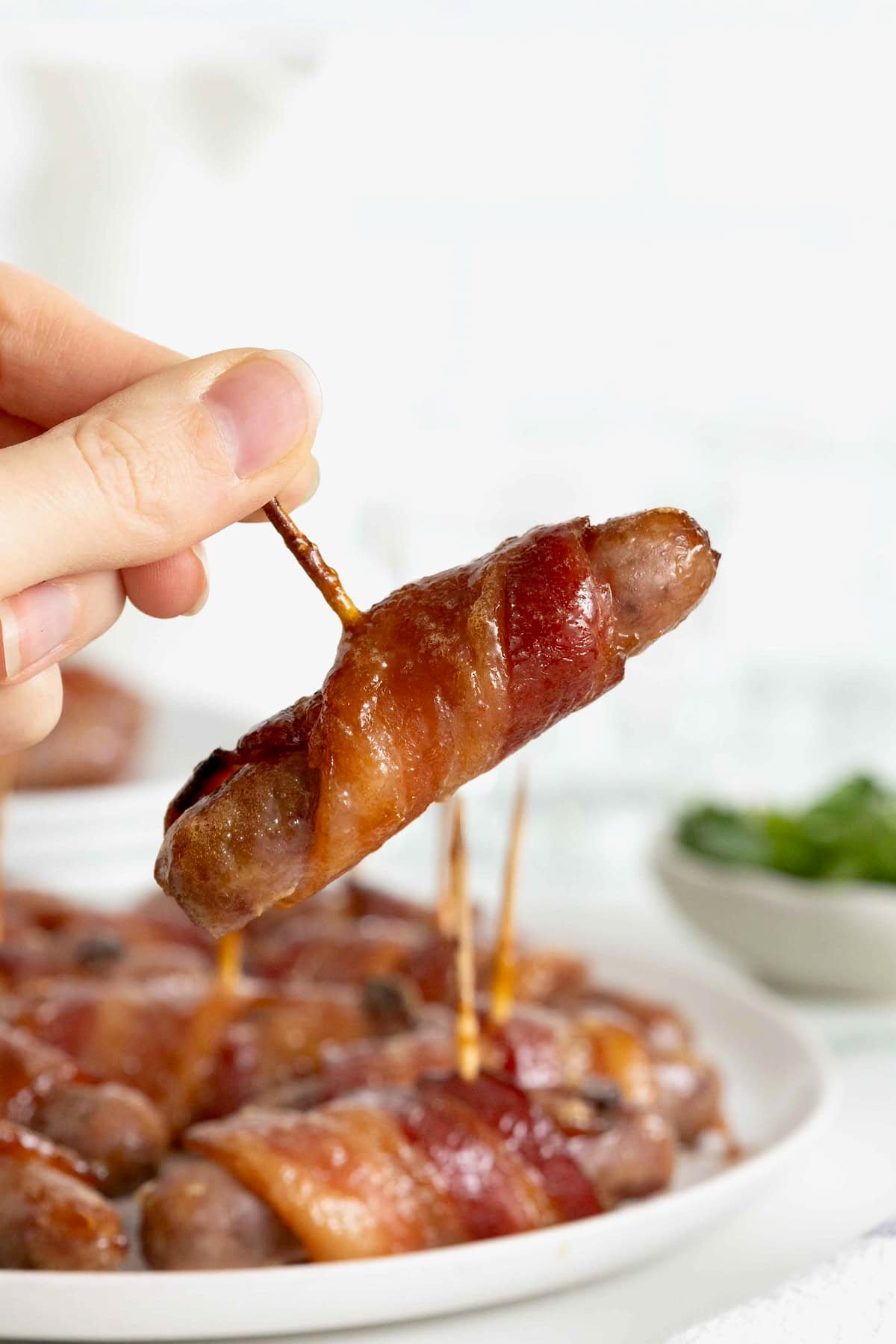 A breakfast sausage wrapped in bacon being picked up by a toothpick.
