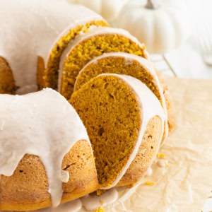 A chai spiced pumpkin pound cake sliced and sitting on a parchment lined gold toned cooling rack. There are white mini pumpkins in the background.