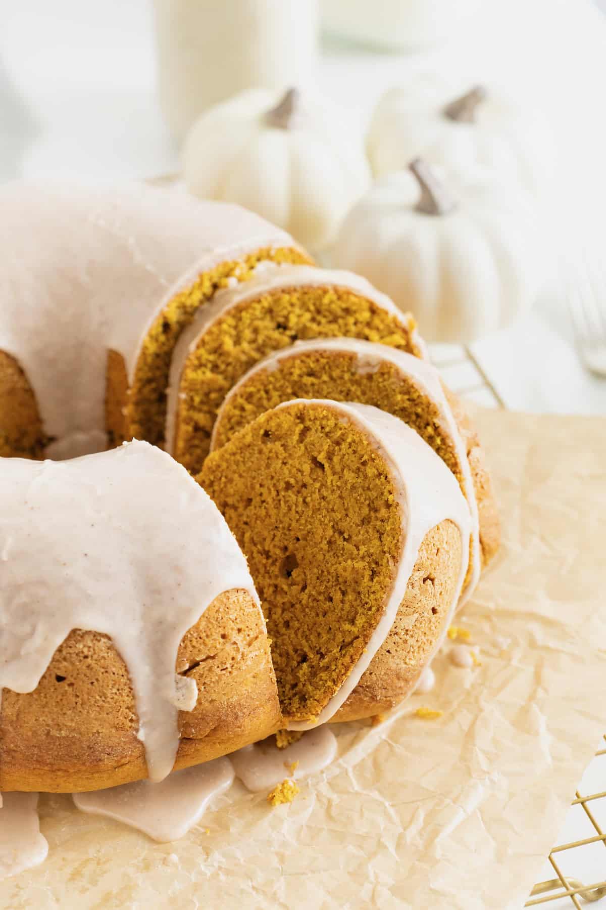 A chai spiced pumpkin pound cake sliced and sitting on a parchment lined gold toned cooling rack. There are white mini pumpkins in the background.