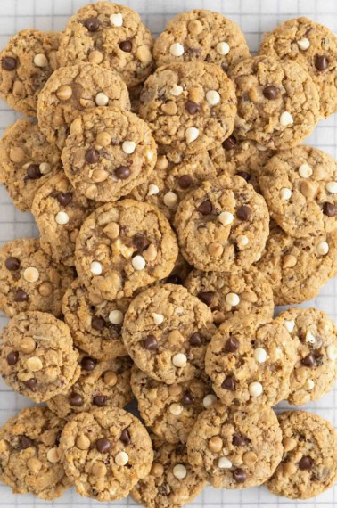 A pile of cookies on a parchment lined cooling rack. The cookies have mini marshmallows, chocolate chips and butterscotch chips.