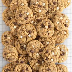 A pile of cookies on a parchment lined cooling rack. The cookies have white chocolate, chocolate chips and butterscotch chips.