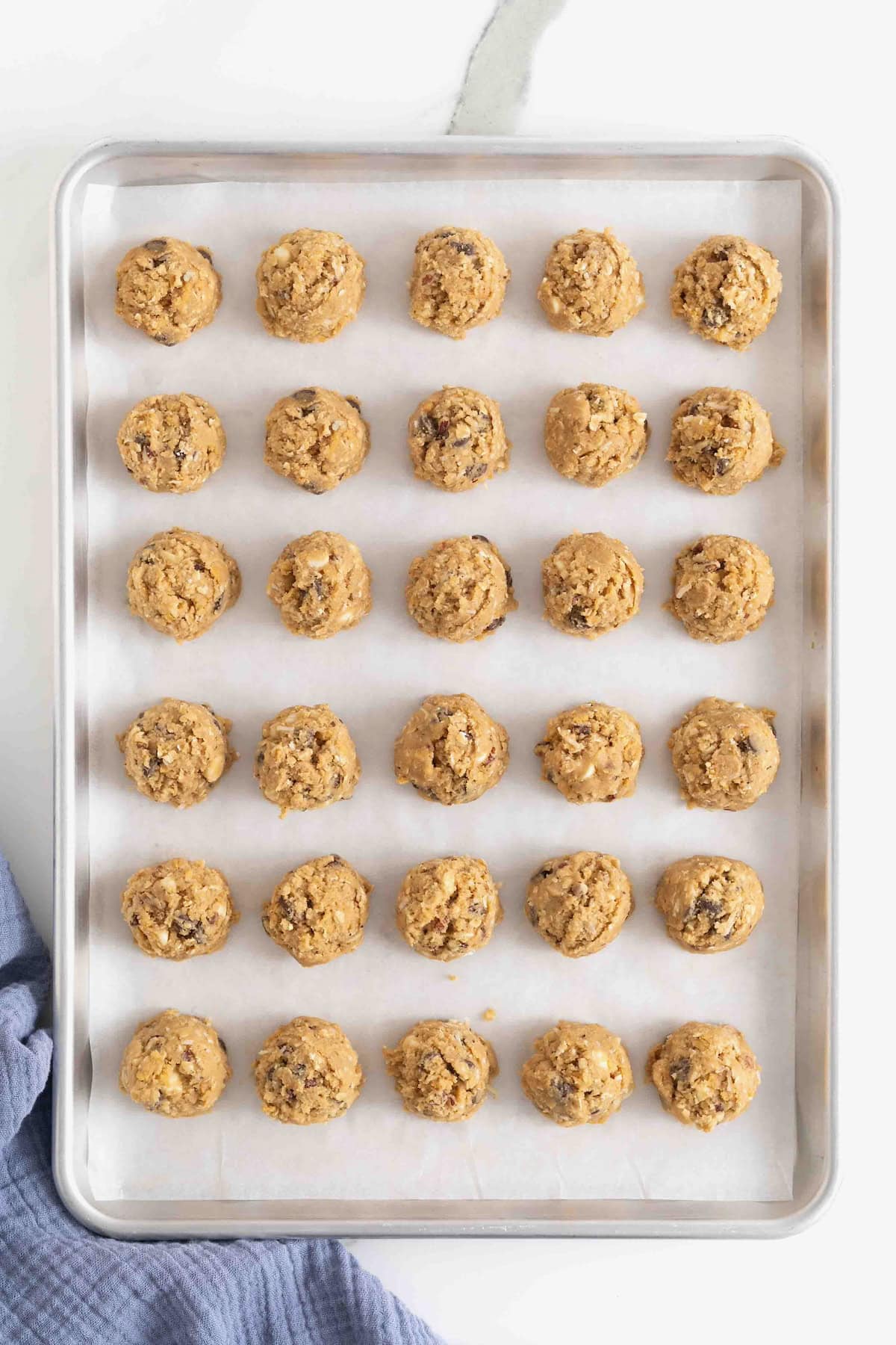 30 balls of cookie dough on a parchment lined aluminum baking sheet.