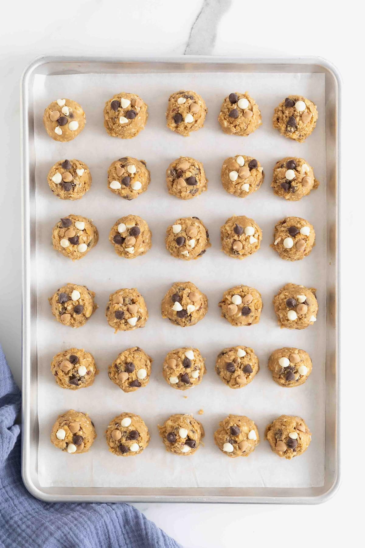30 balls of cookie dough on a parchment lined aluminum baking sheet. 