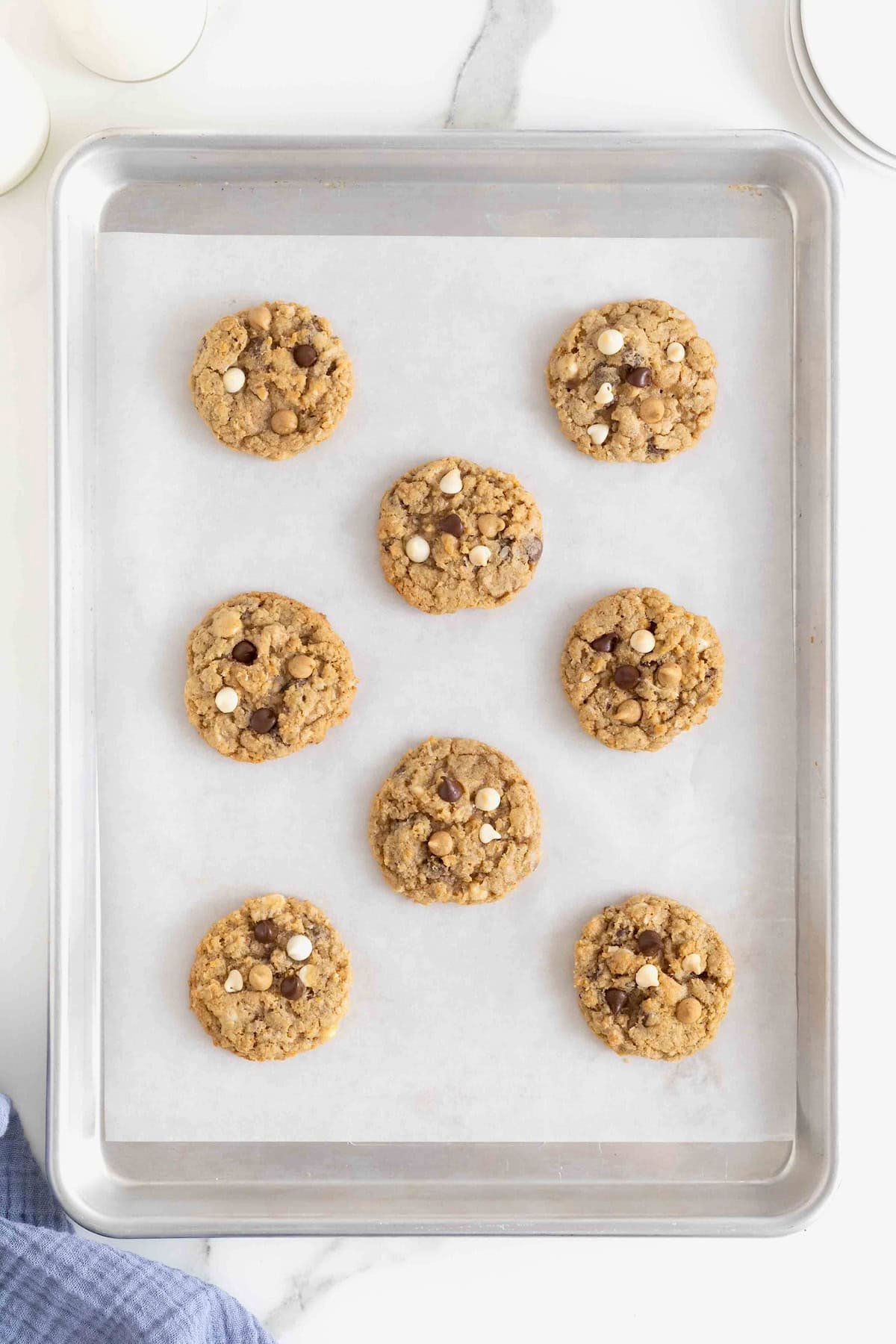 Eight cowboy cookies on a parchment lined aluminum baking sheet.