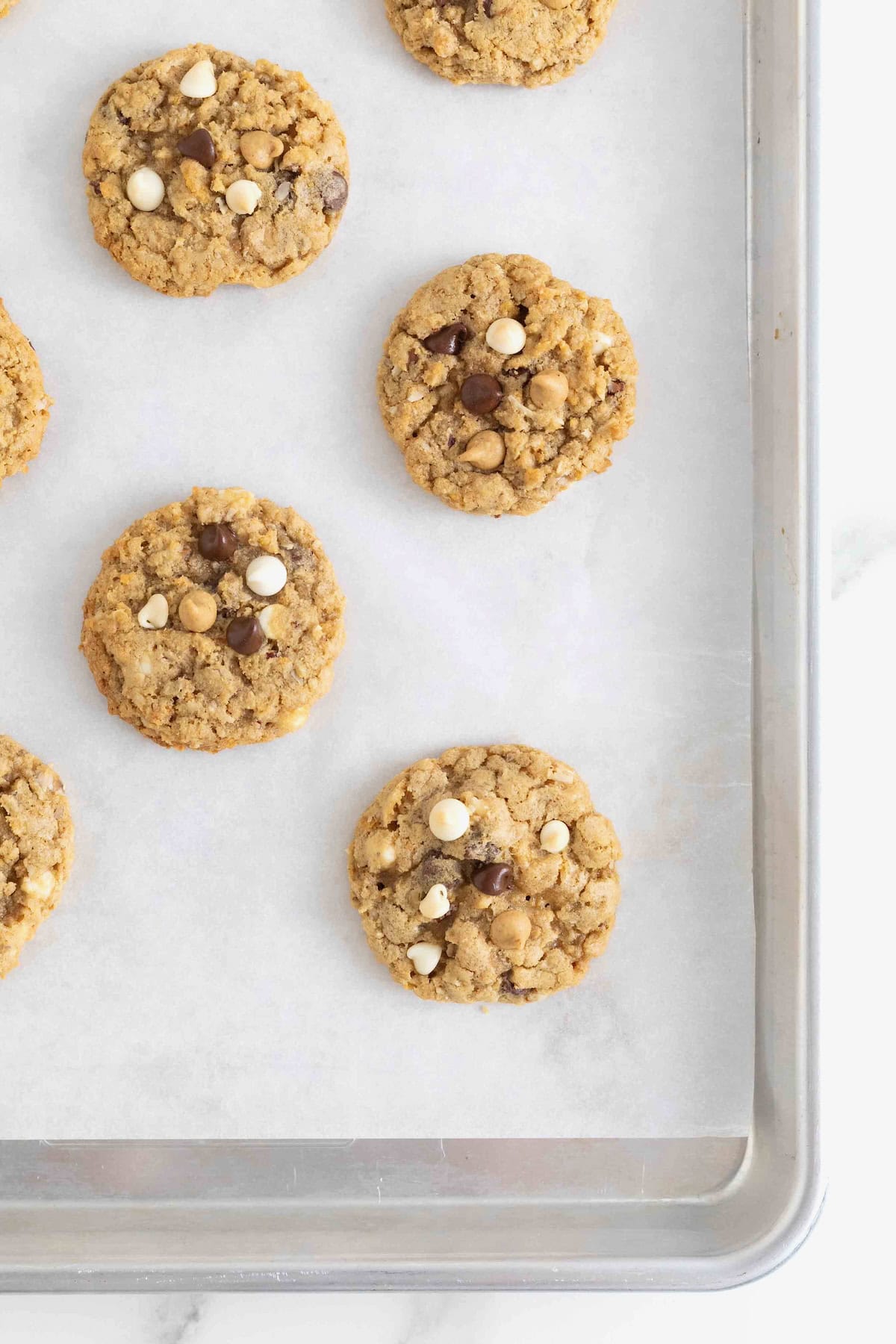Five cowboy cookies on a parchment lined aluminum baking sheet.