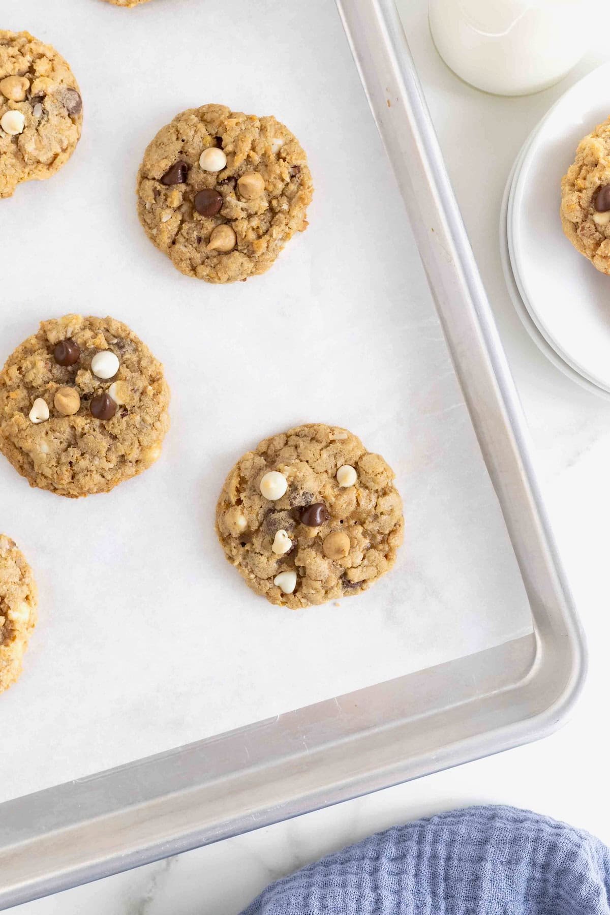 Five cowboy cookies on a parchment lined aluminum baking sheet.