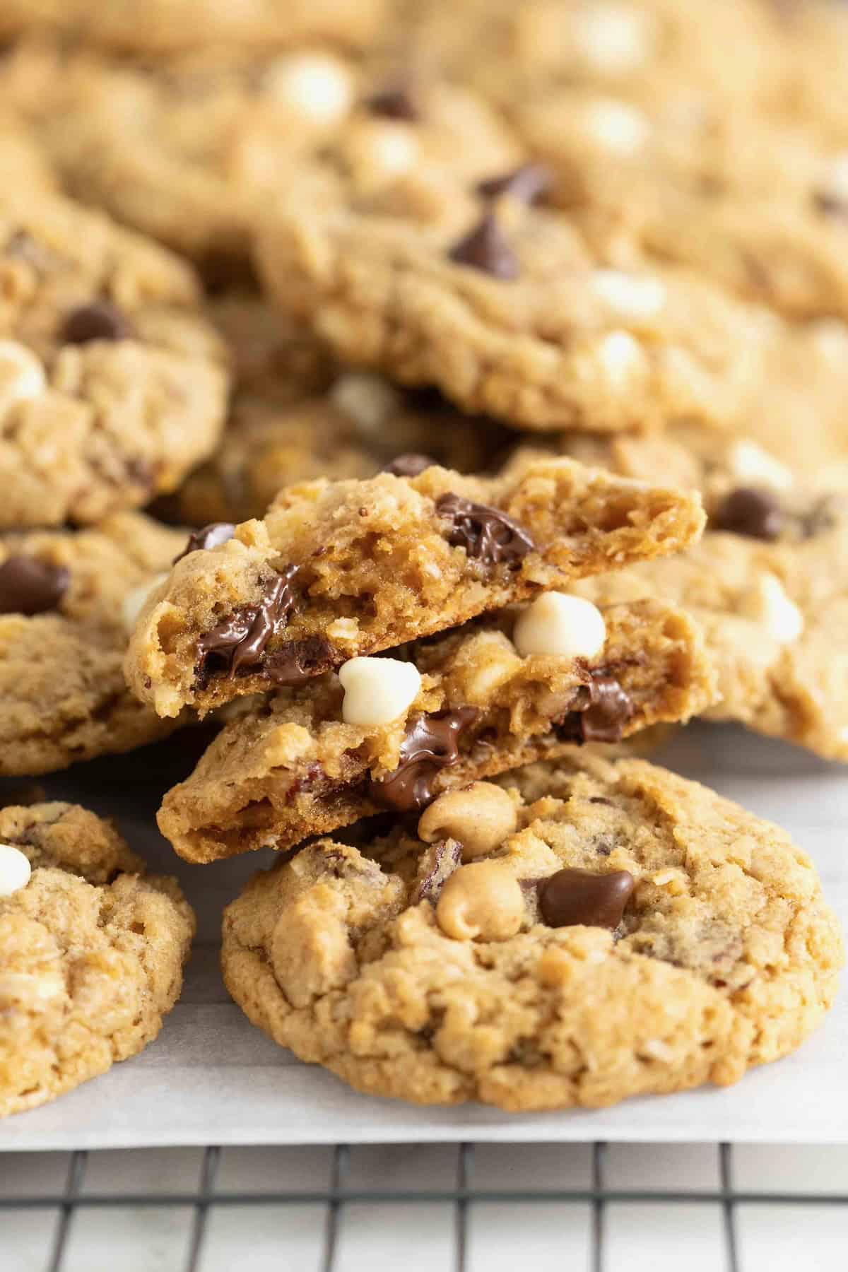A pile of cowboy cookies on a small white surface. The top cookie has a bite out of it.