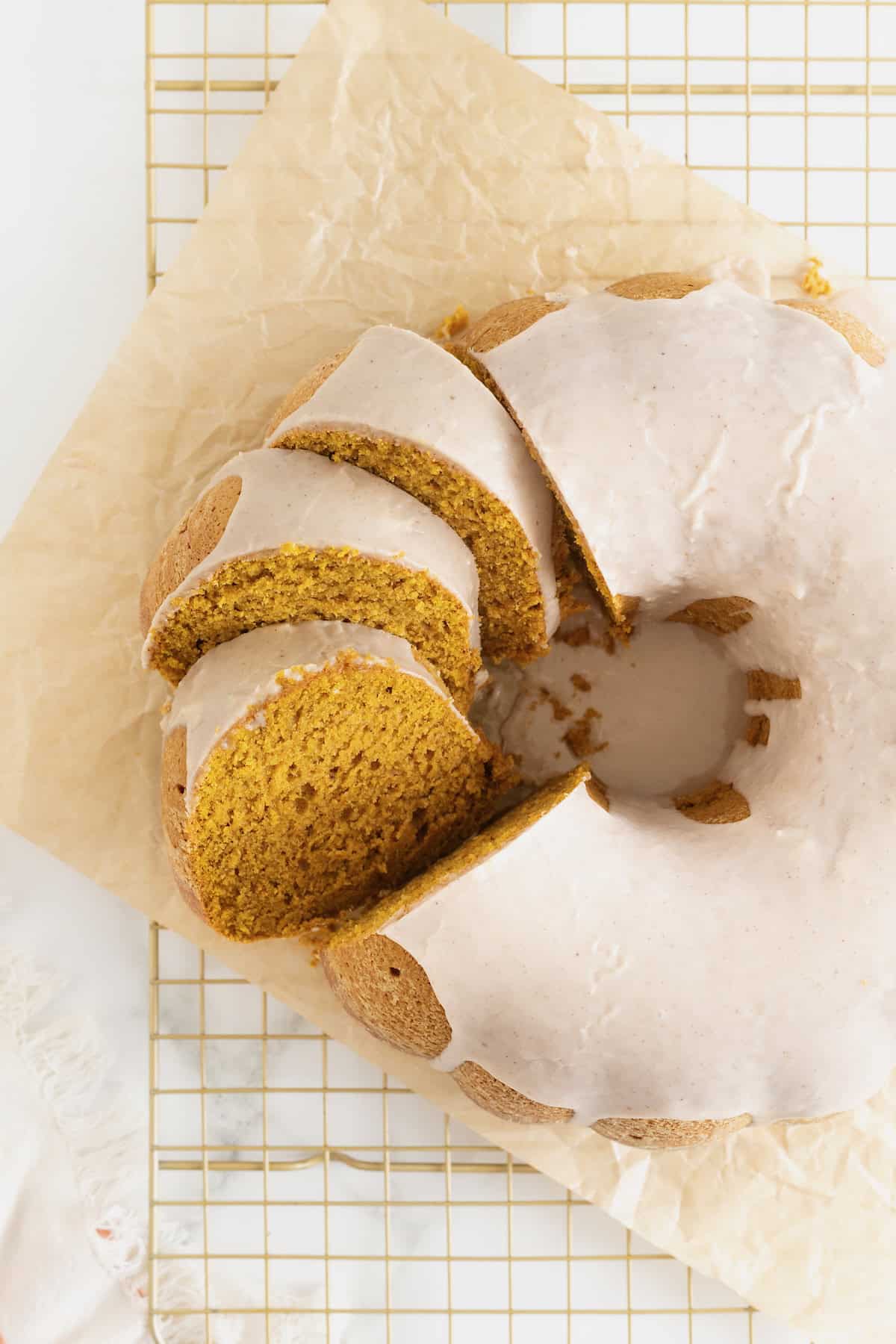A chai spiced pumpkin pound cake sliced and sitting on a parchment lined gold toned cooling rack.