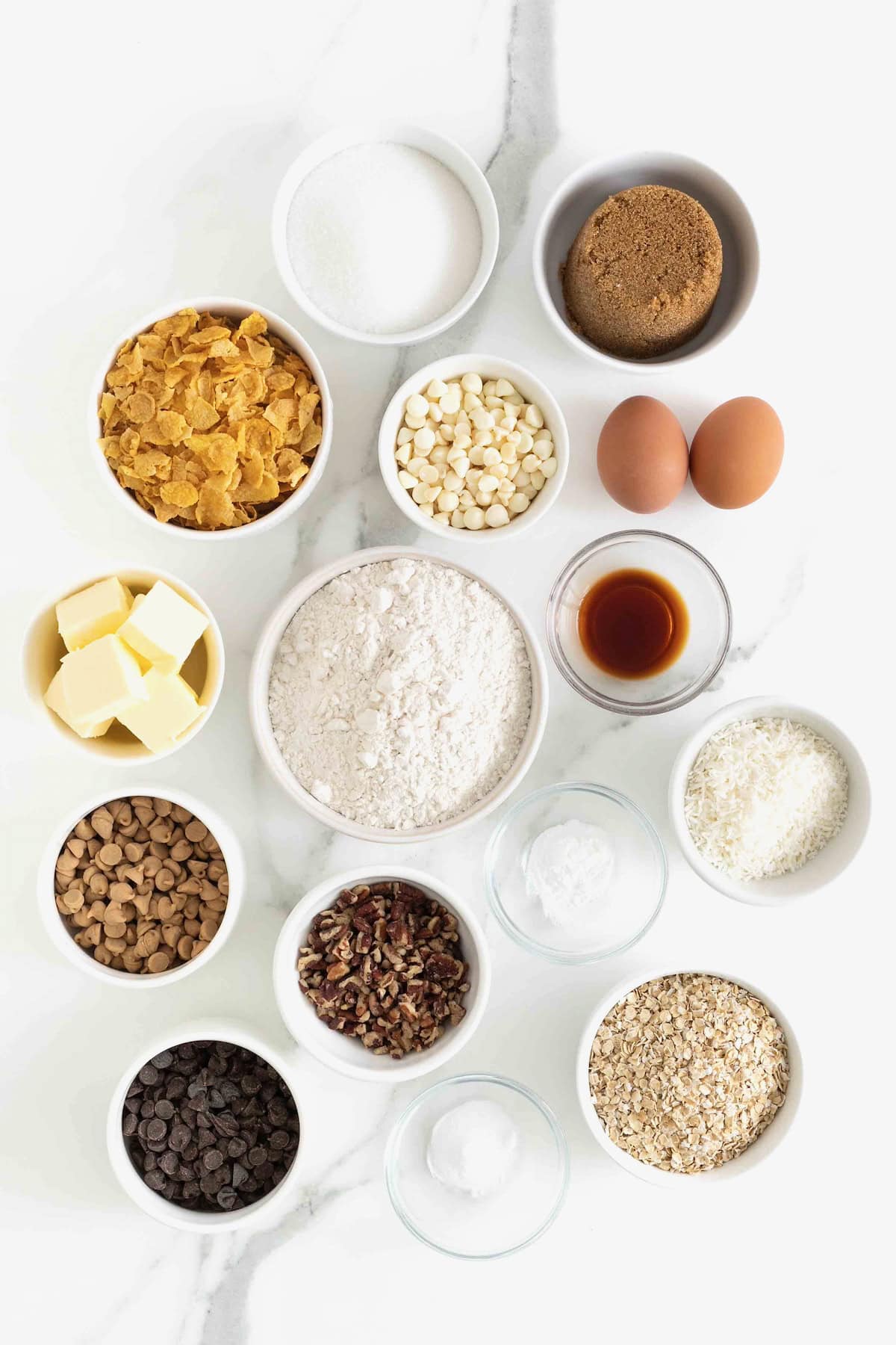 Ingredients to make Cowboy Cookies in small white dishes on a white marble counter.