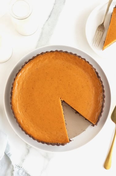 A pumpkin tart with a chocolate crust on a white serving plate. There is a slice of tart missing.