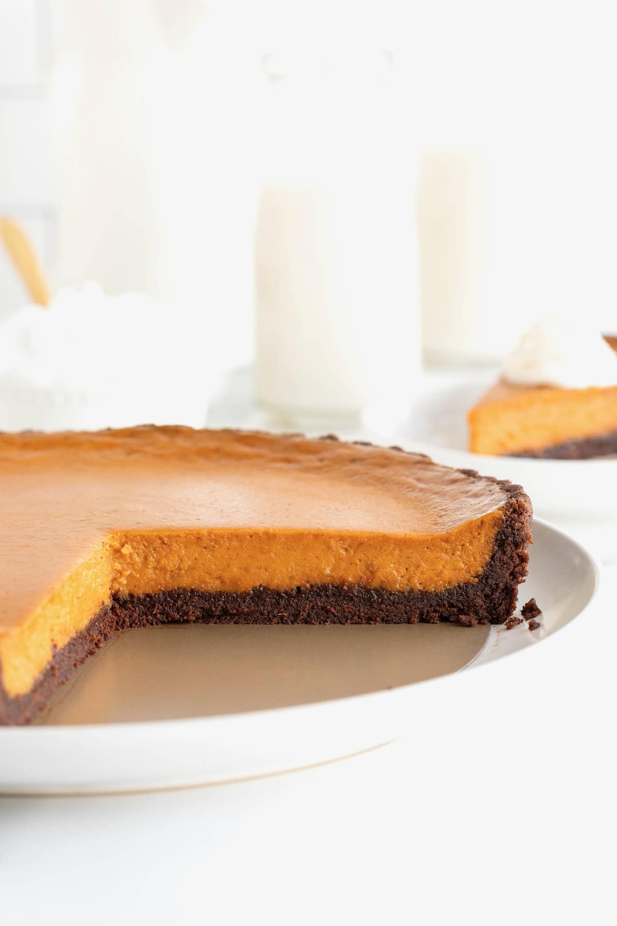 A pumpkin tart with a chocolate crust on a white serving plate. There is a wedge of tart missing.