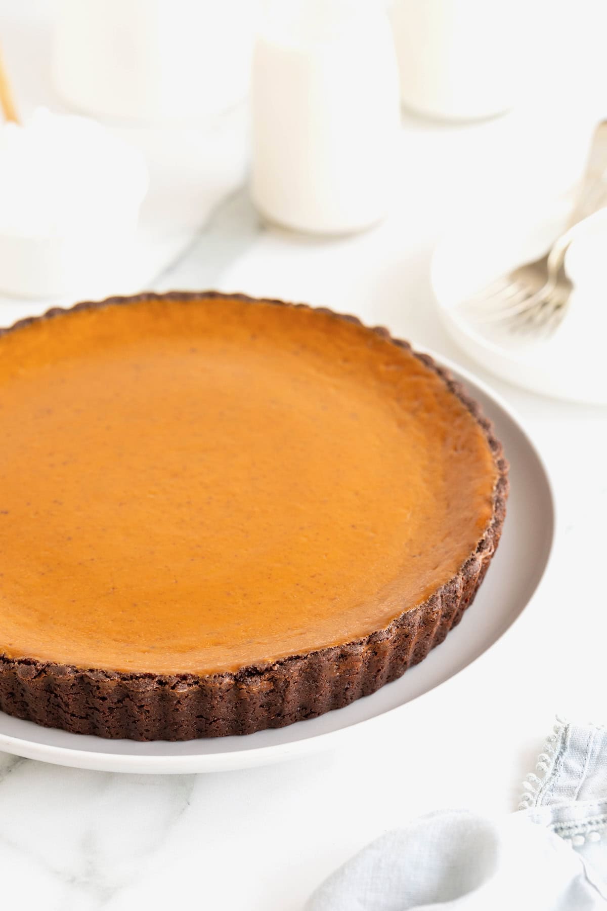 A pumpkin tart with a chocolate crust on a white serving plate. 