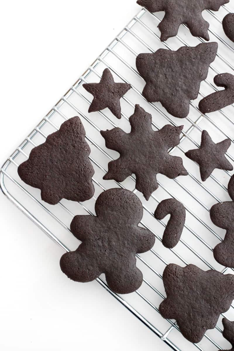 A metal cooling rack with chocolate Christmas shaped cookies of various sizes.