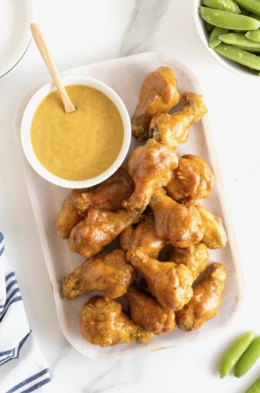 A long white serving plate filled with honey mustard chicken wings and a small round dish of honey mustard sauce.