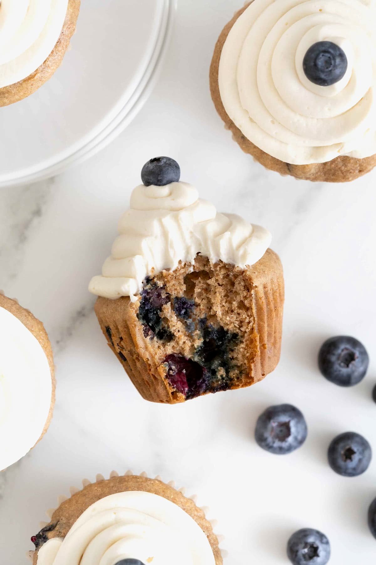 A blueberry cupcake with a bite taken out of it laying on a white surface.