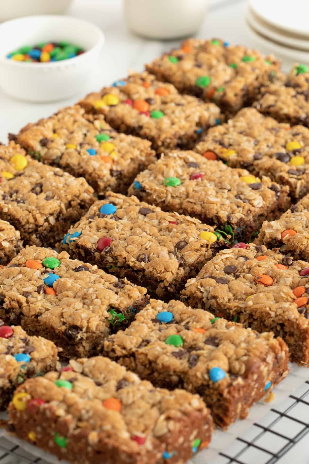 Monster cookie bars on a parchment lined metal cooling rack. There's a bowl of mini m&ms in the background.