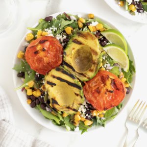 A grilled avocado and tomato salad on a large white plate.