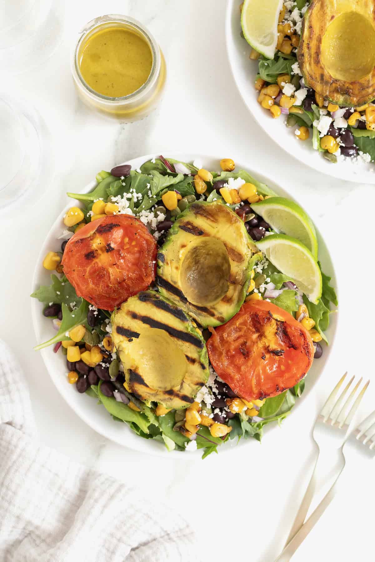 A grilled avocado and tomato salad on a large white plate.