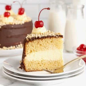 A slice of hot fudge sundae cake topped with a maraschino cherry on a small white plate.