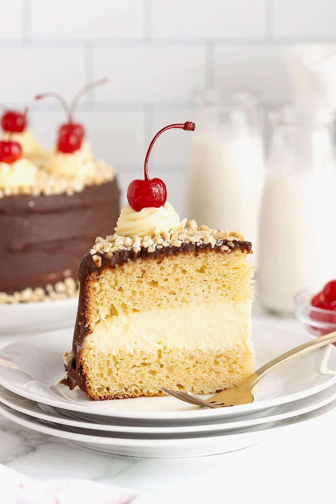 A slice of hot fudge sundae cake topped with a maraschino cherry on a small white plate.