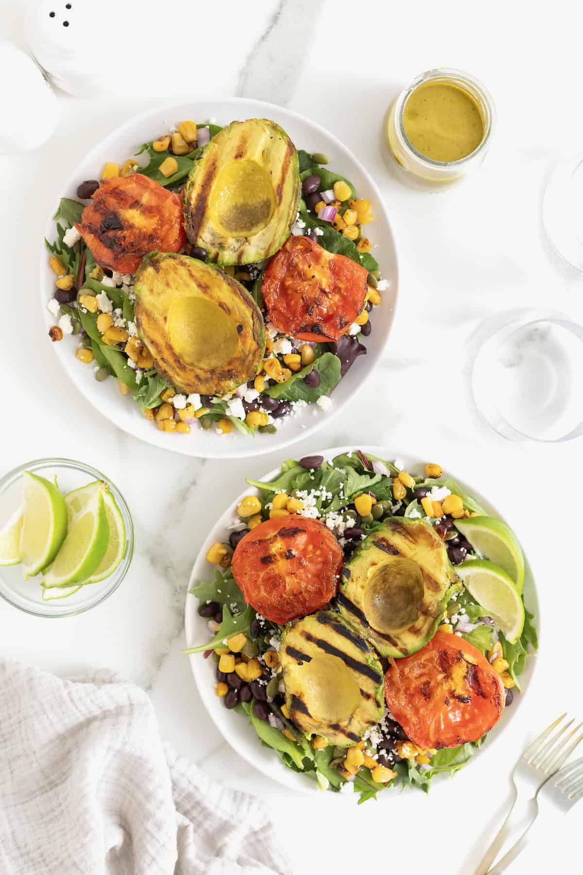 A grilled avocado and tomato salad on a large white plate.