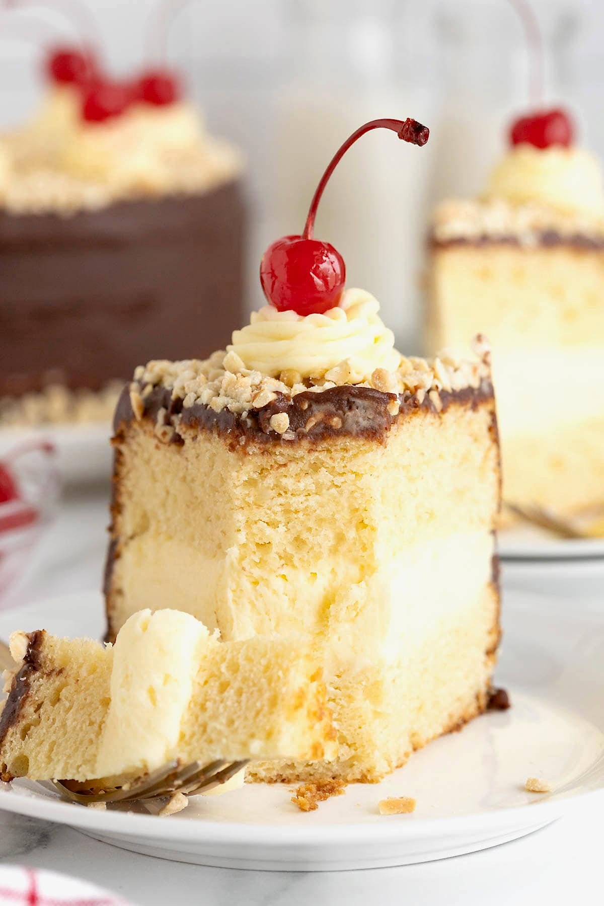 A slice of hot fudge sundae cake topped with a maraschino cherry on a small white plate. A bite has been taken out of the cake.