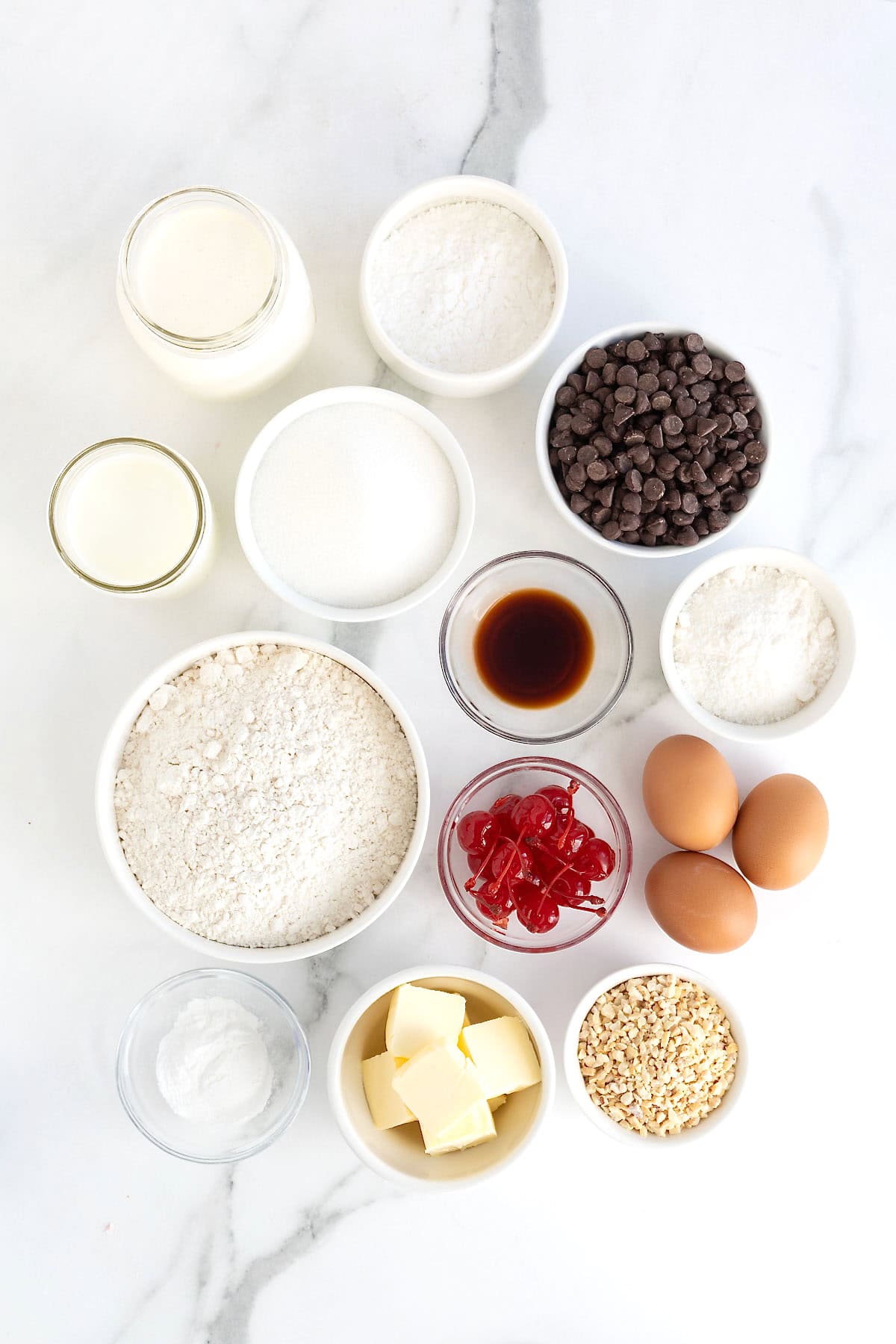 Ingredients to make a hot fudge sundae cake in small white dishes on a white marble counter.