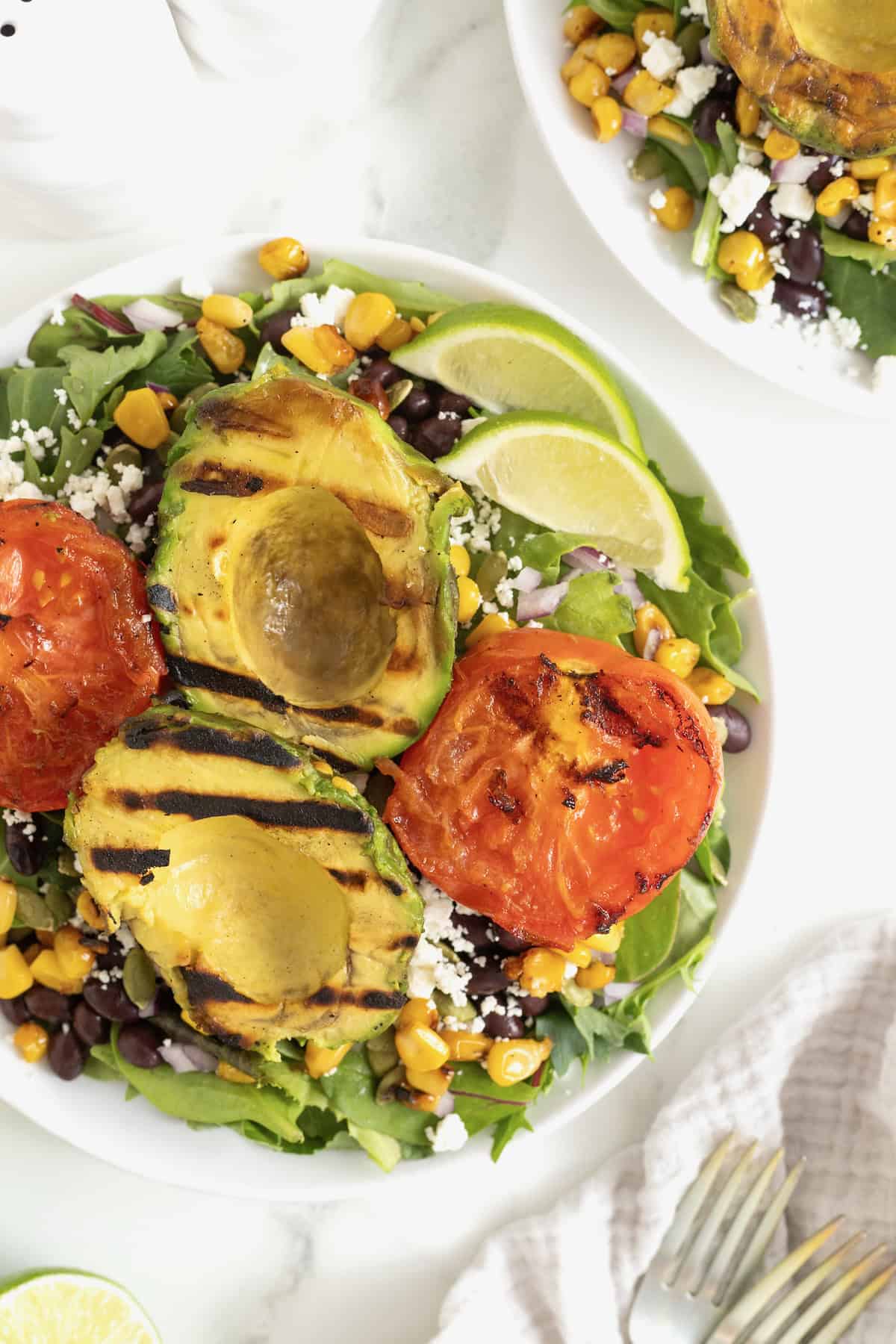 A grilled avocado and tomato salad on a large white plate.