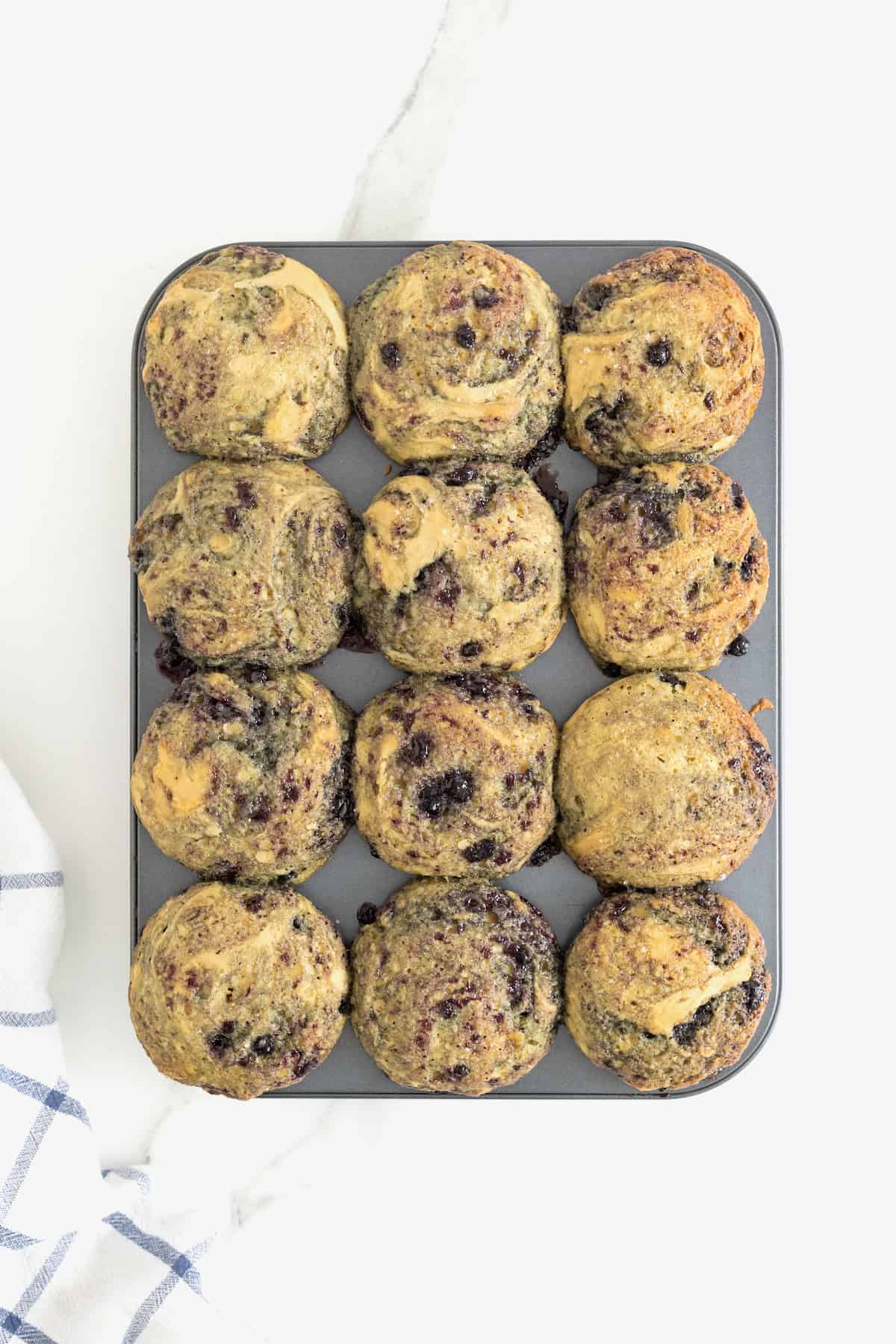 Blueberry swirled muffins baked in an aluminum muffin pan.