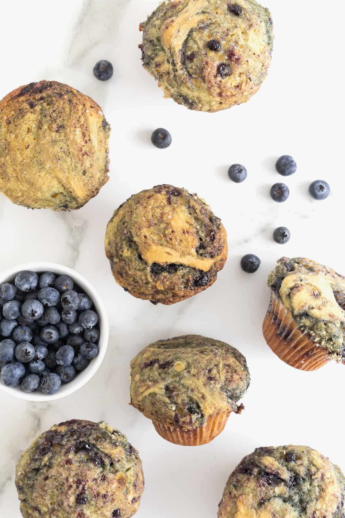 Blueberry swirled muffins on a white marble counter.