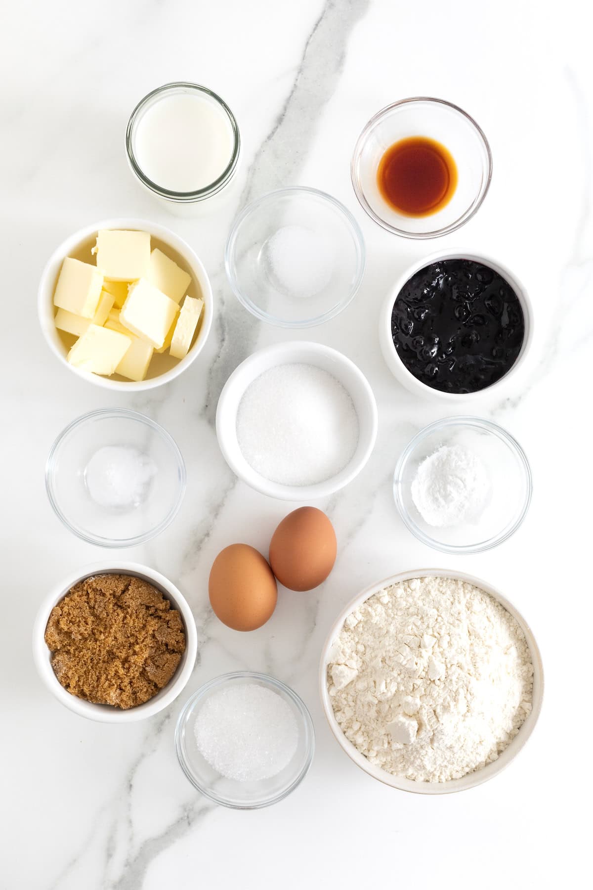Ingredients to make blueberry swirl muffins in small glass dishes on a white marble counter.