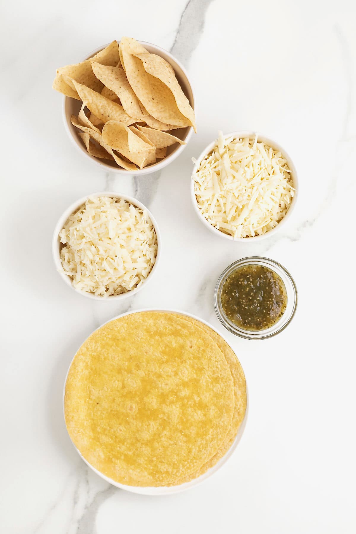 Ingredients to make skillet queso fundido in small glass dishes on a white marble counter.