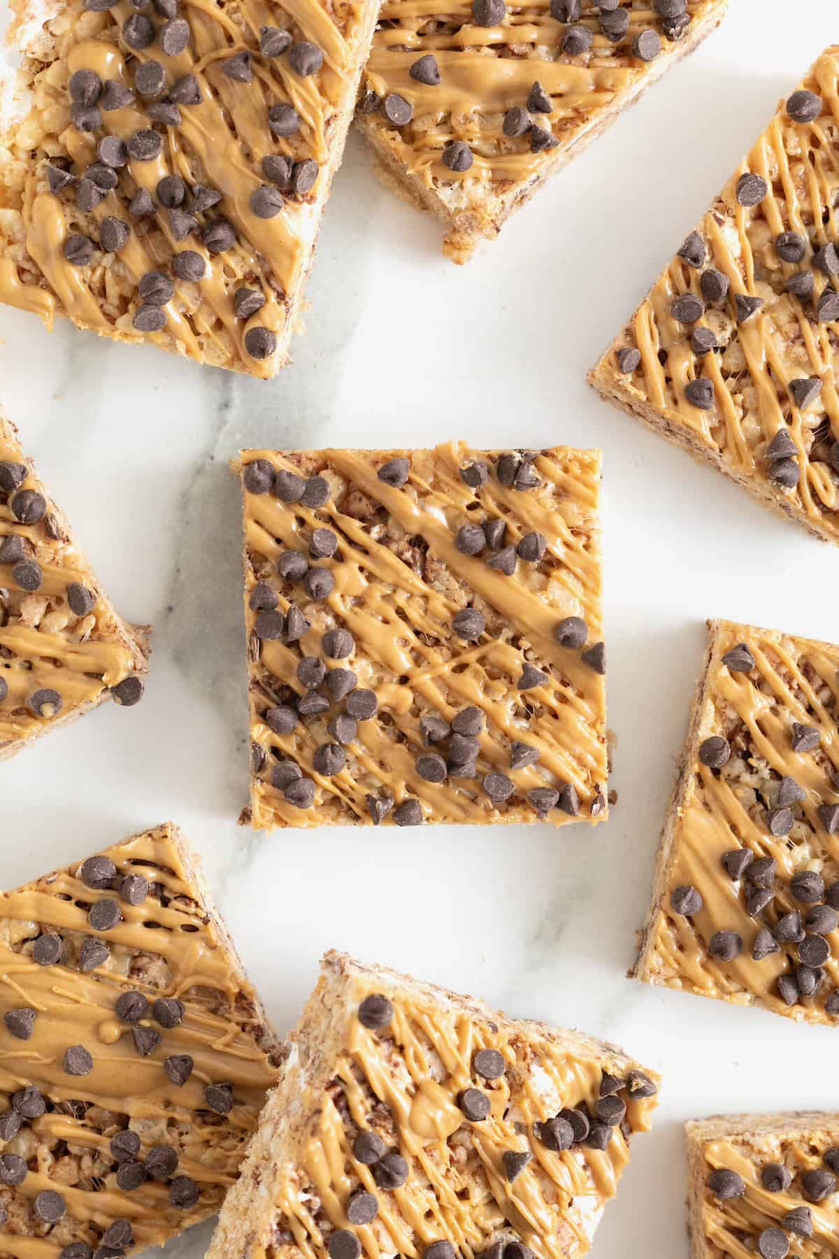 Eight chocolate chip peanut butter Rice Krispies treats on a white marble counter.