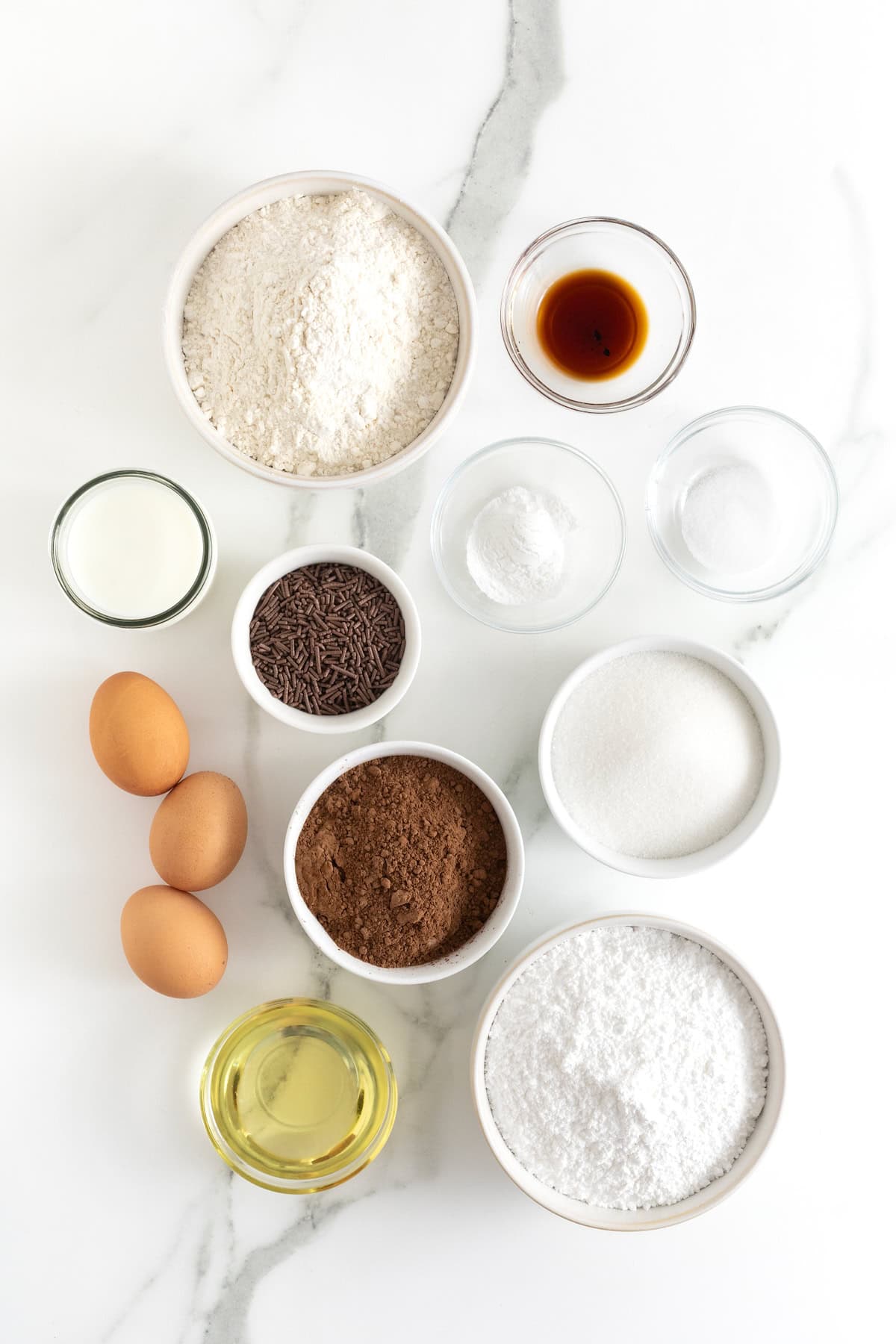 Ingredients to make triple chocolate baked donuts in small glass dishes on a white counter.