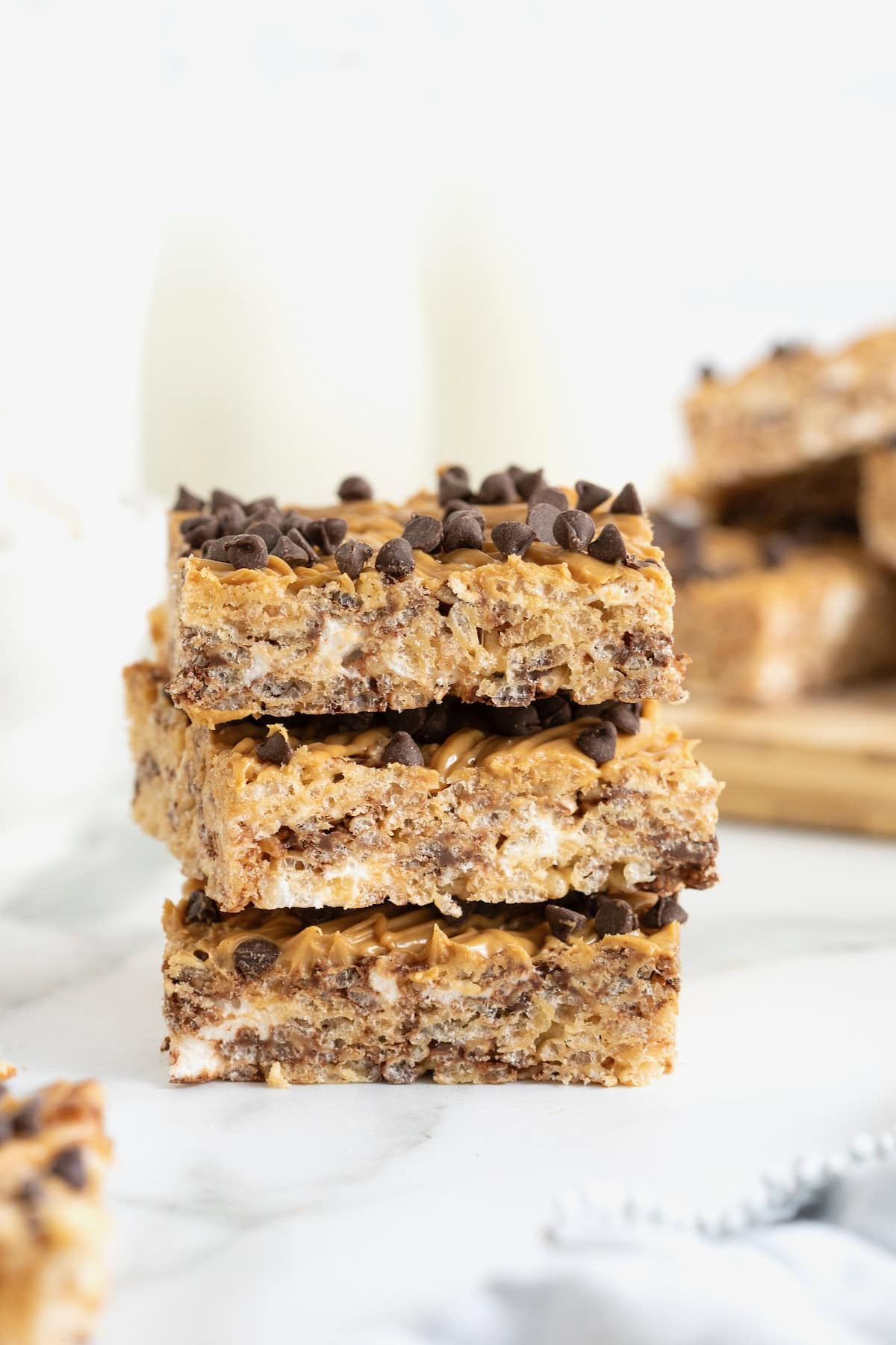 A stack of three peanut butter chocolate chip Rice Krispies treats on a white marble counter.