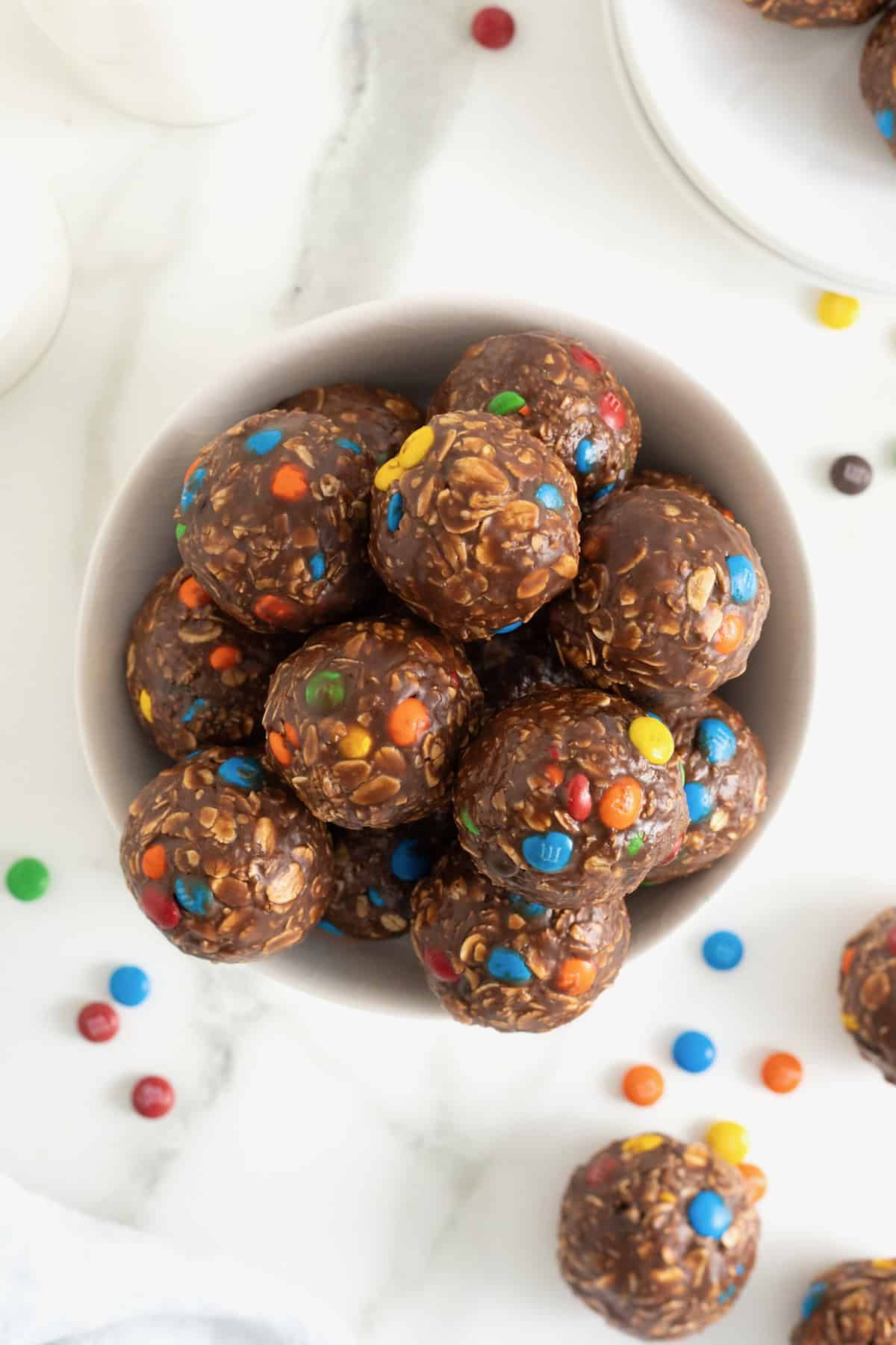 A white bowl of Nutella M&M oatmeal balls on a white marble counter.