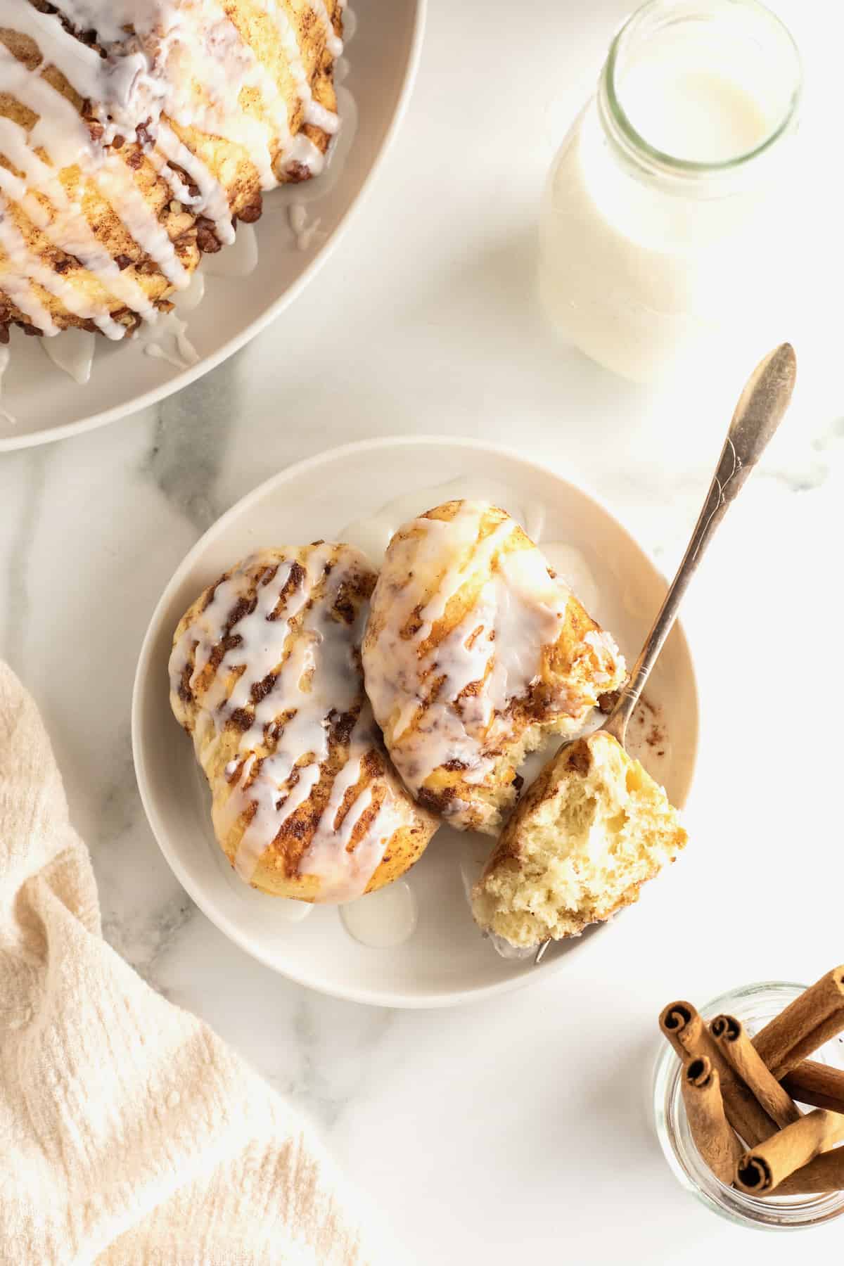 Two sweet rolls covered in glaze and chopped pecans on a white plate with a fork.