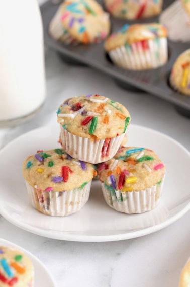 Three birthday breakfast muffins with colorful sprinkles on a white plate.