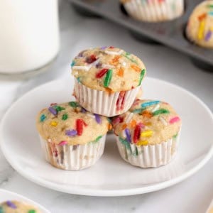 Three birthday breakfast muffins with colorful sprinkles on a white plate.