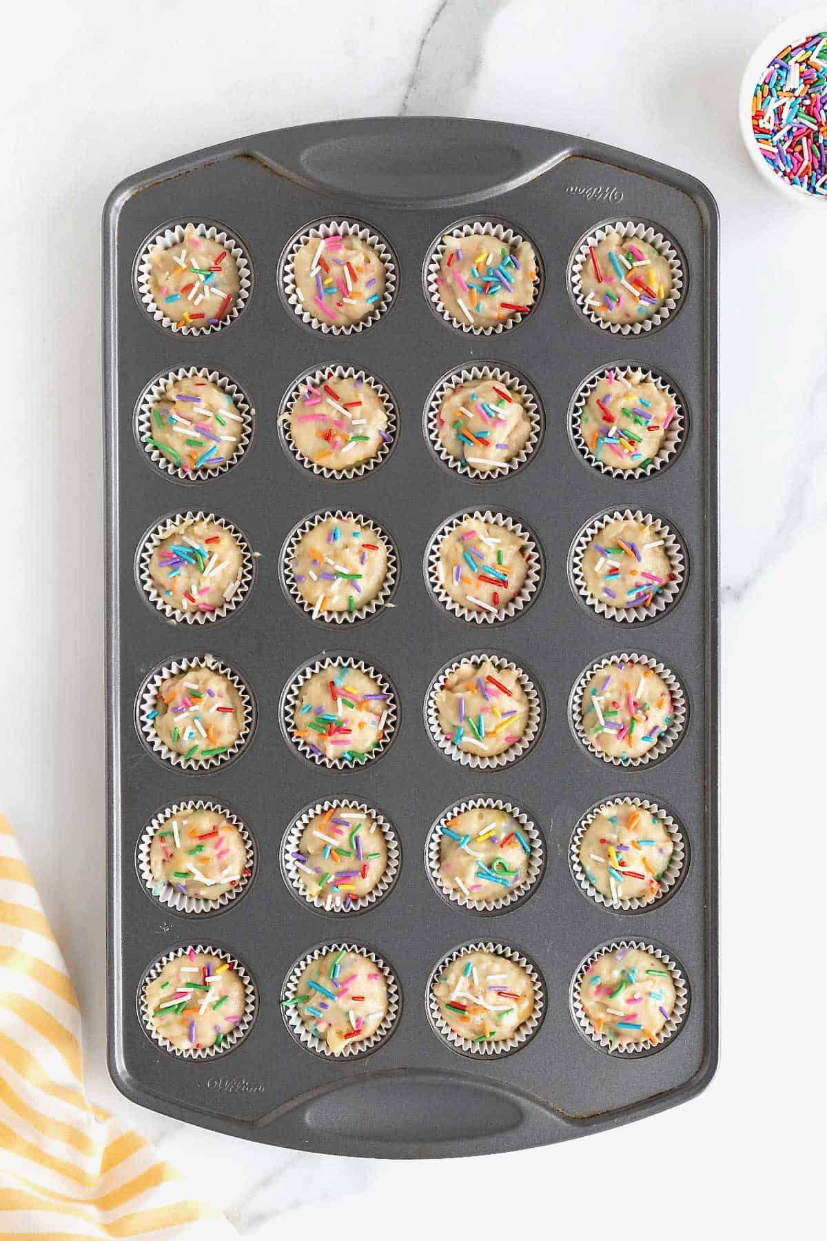 Confetti muffin batter in a dark aluminum mini muffin pan.
