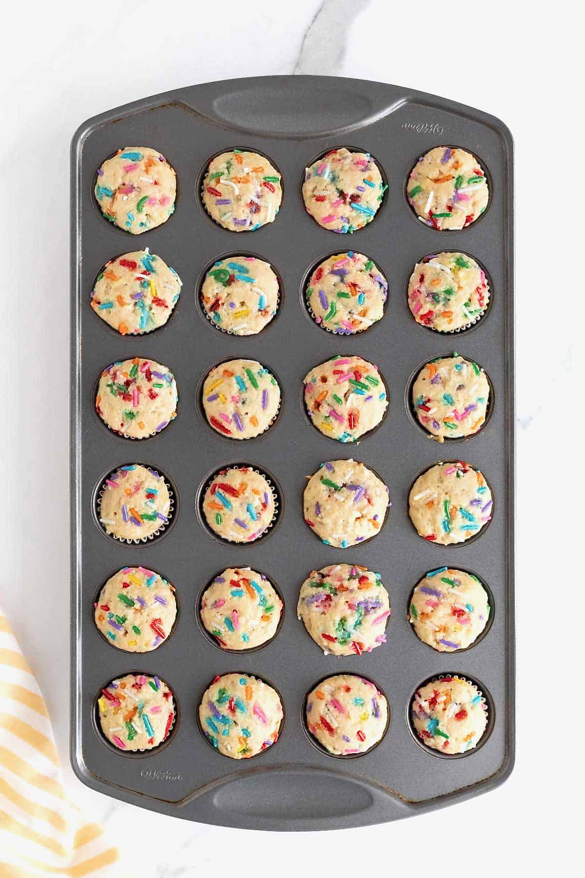 Confetti muffins baked in a dark aluminum mini muffin pan.