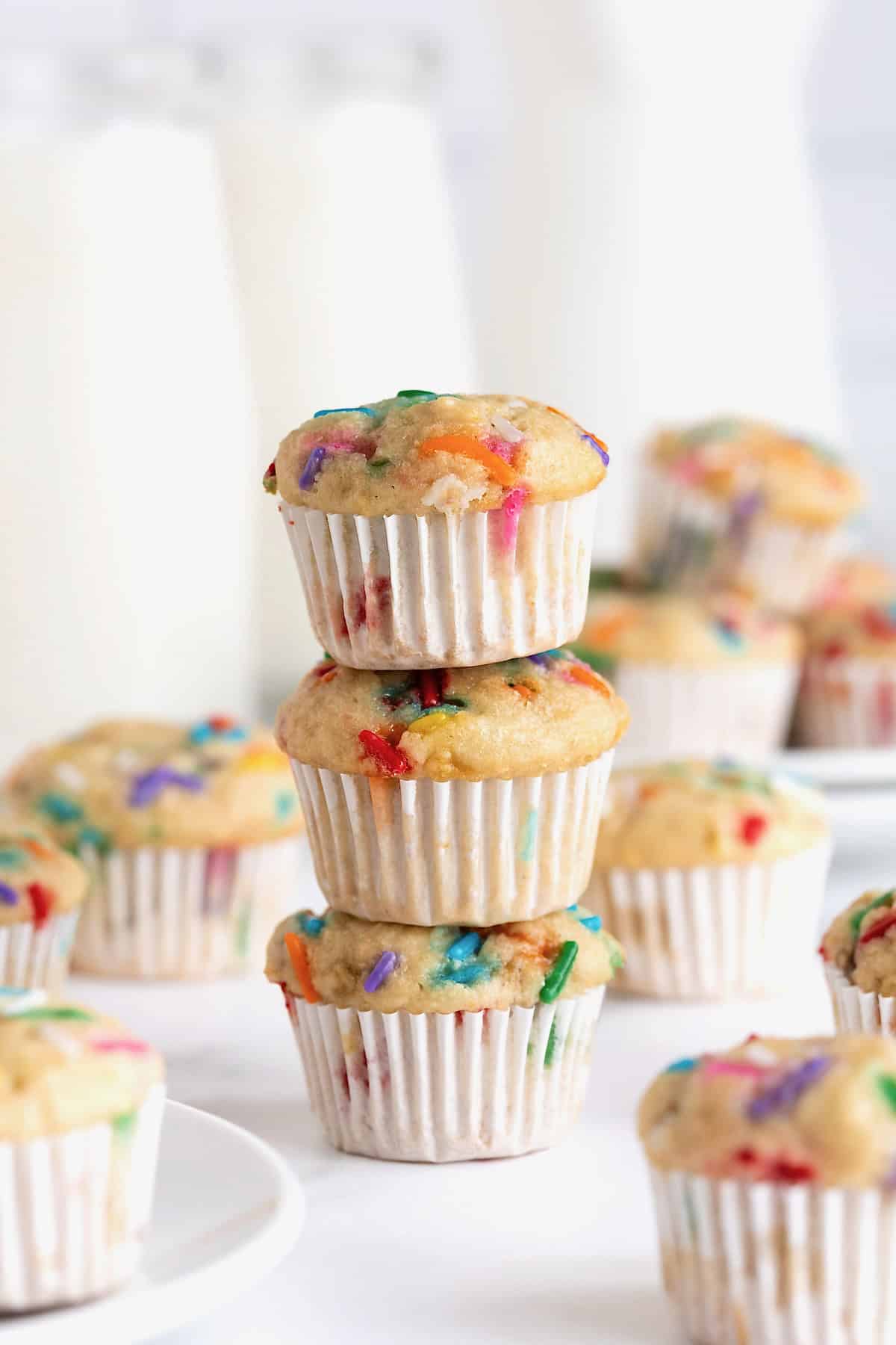 Three confetti mini muffins stacked on a white counter.