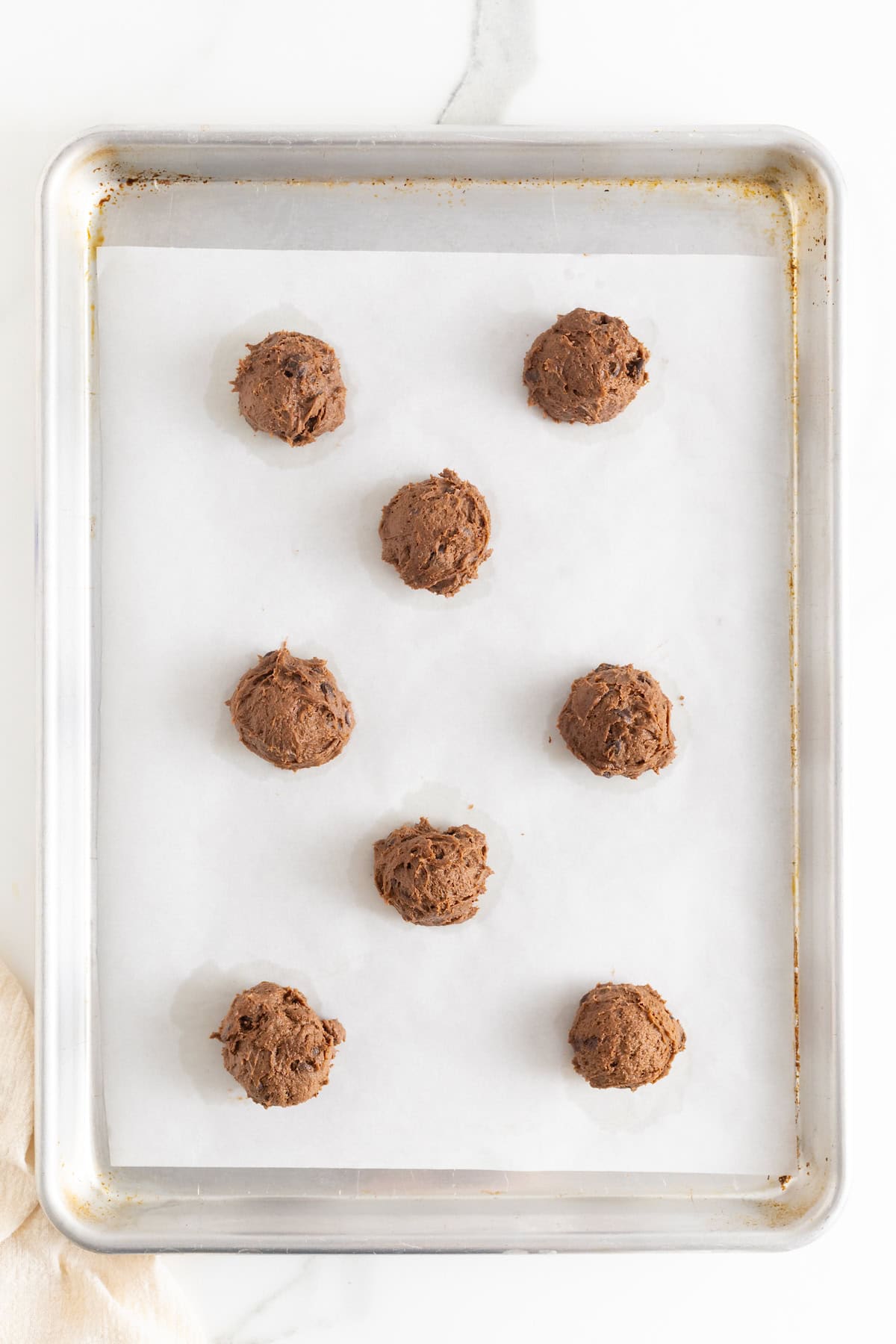 Eight scoops of triple chocolate pumpkin cookie dough on a parchment lined baking sheet.